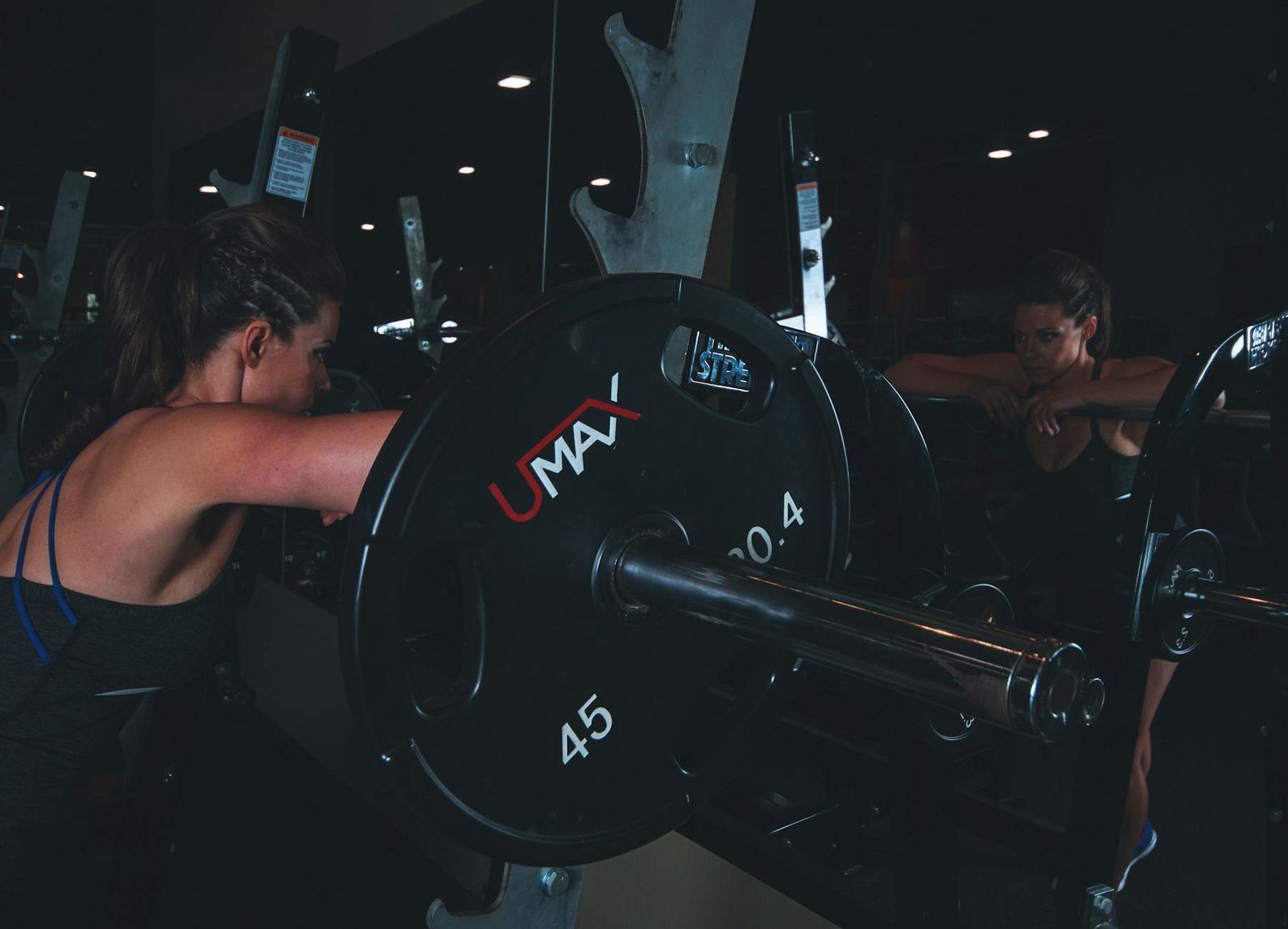 woman leaning on black barbell in front mirror