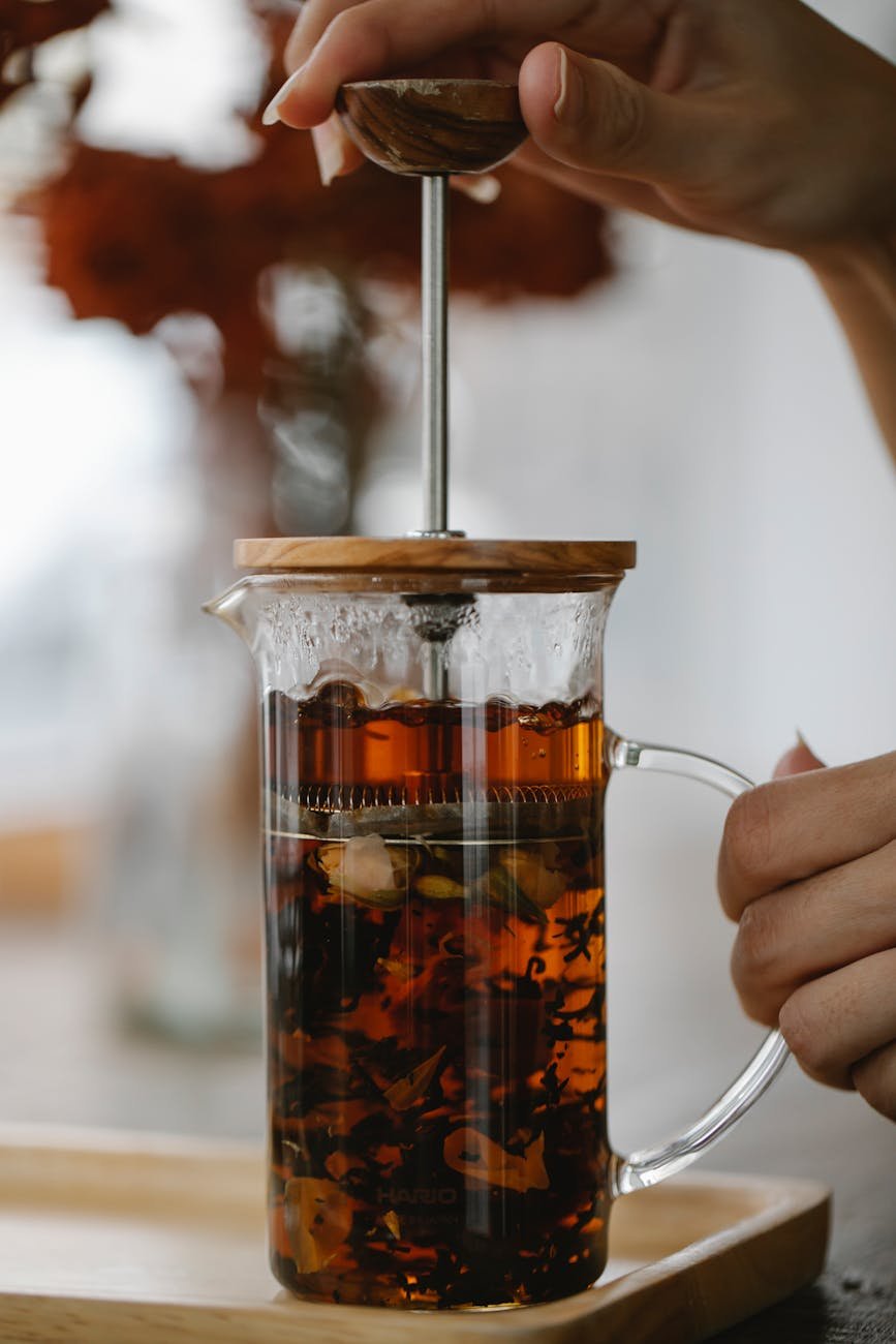 crop unrecognizable woman holding glass french press teapot with tea