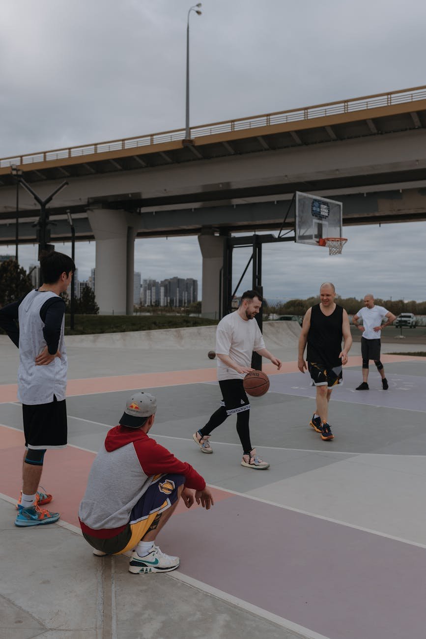 men playing basketball on court near bridge in city